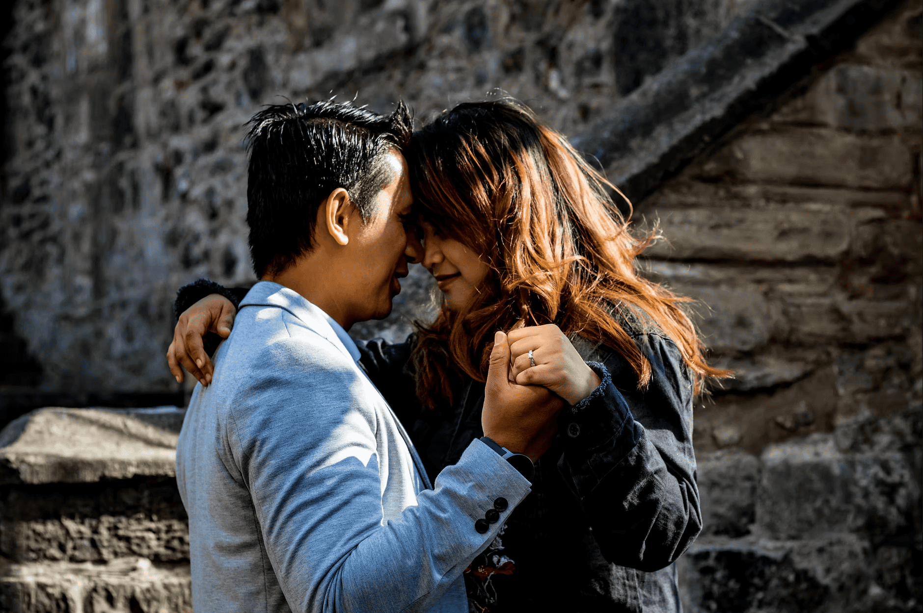 Engaged couple close together in front of ancient castle stonework